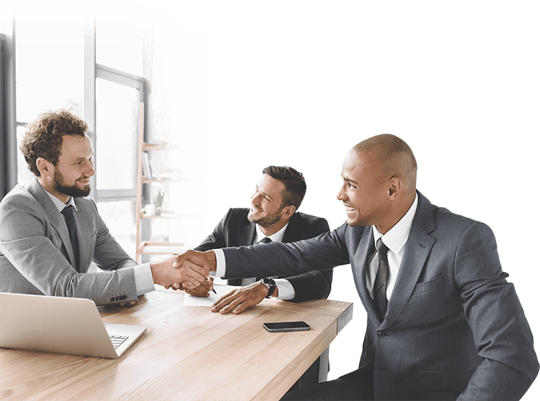 businessmen shaking hands around a conference table with computers and celll phones